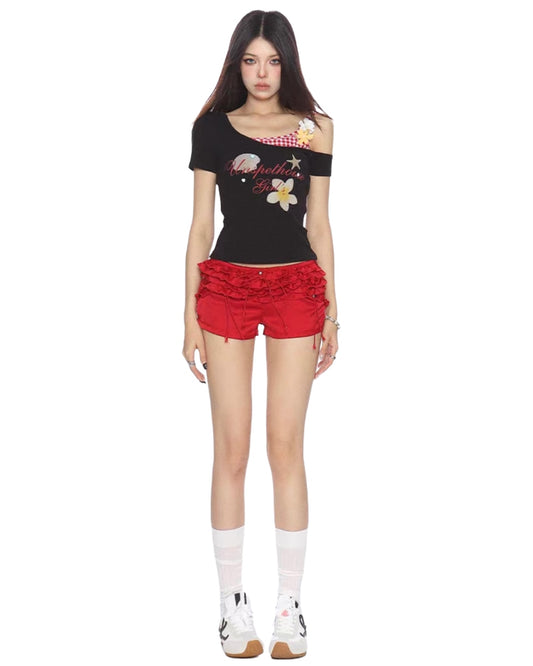 Woman wearing a black top with floral designs and red shorts on a white background