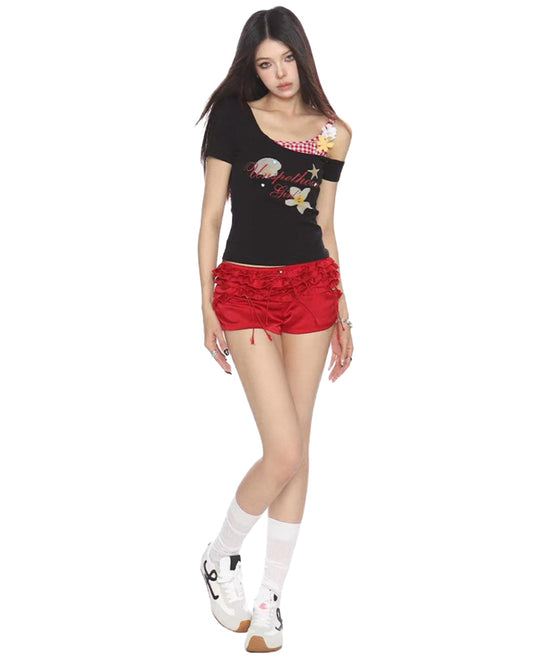 Woman wearing a black top with floral designs and red shorts on a white background