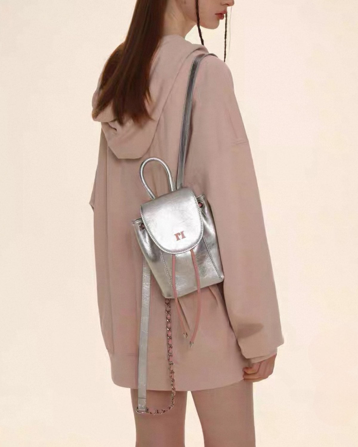 Person wearing a light pink hoodie and carrying a silver backpack on a beige background
