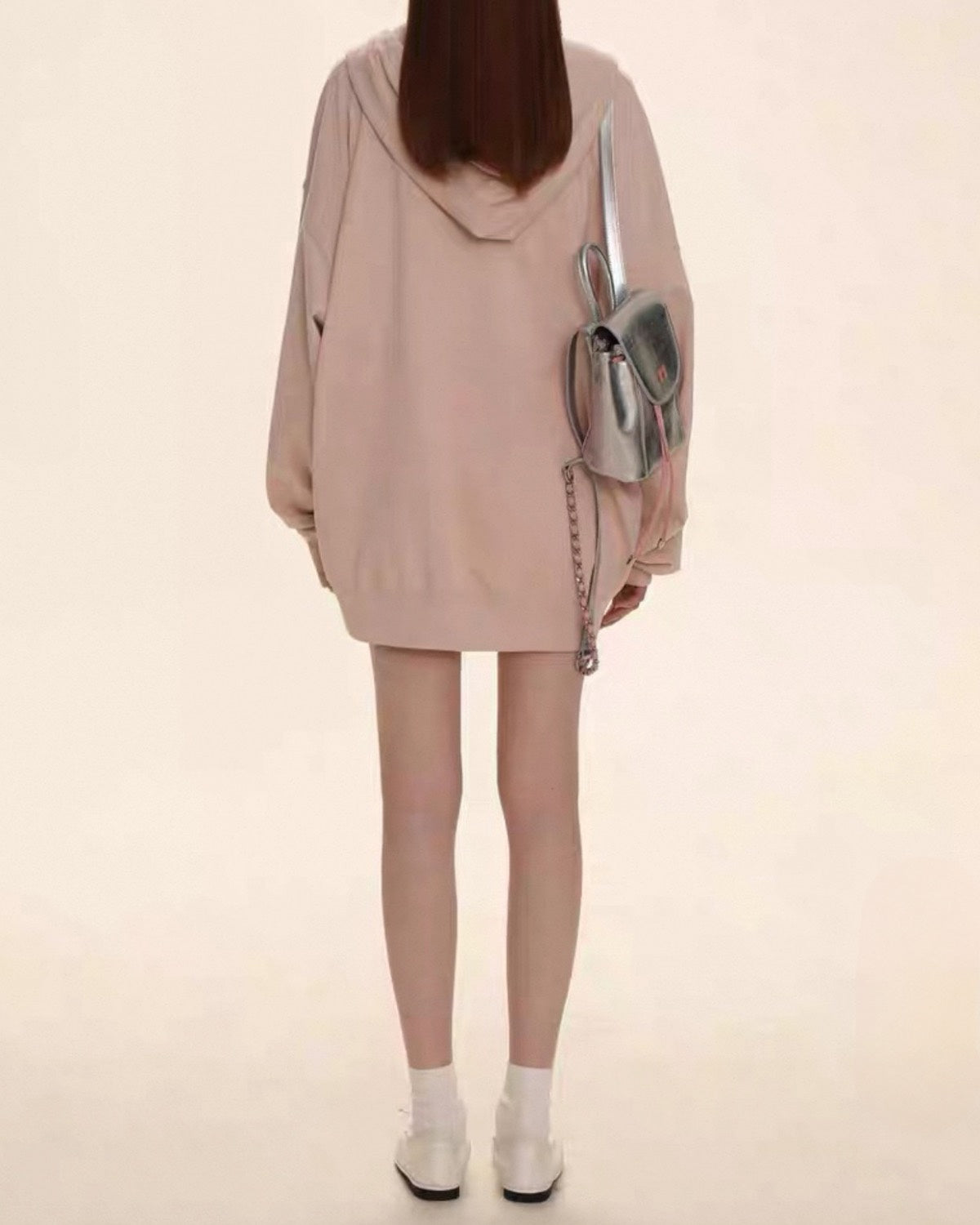 Person wearing a light pink hoodie and skirt with white shoes on a beige background