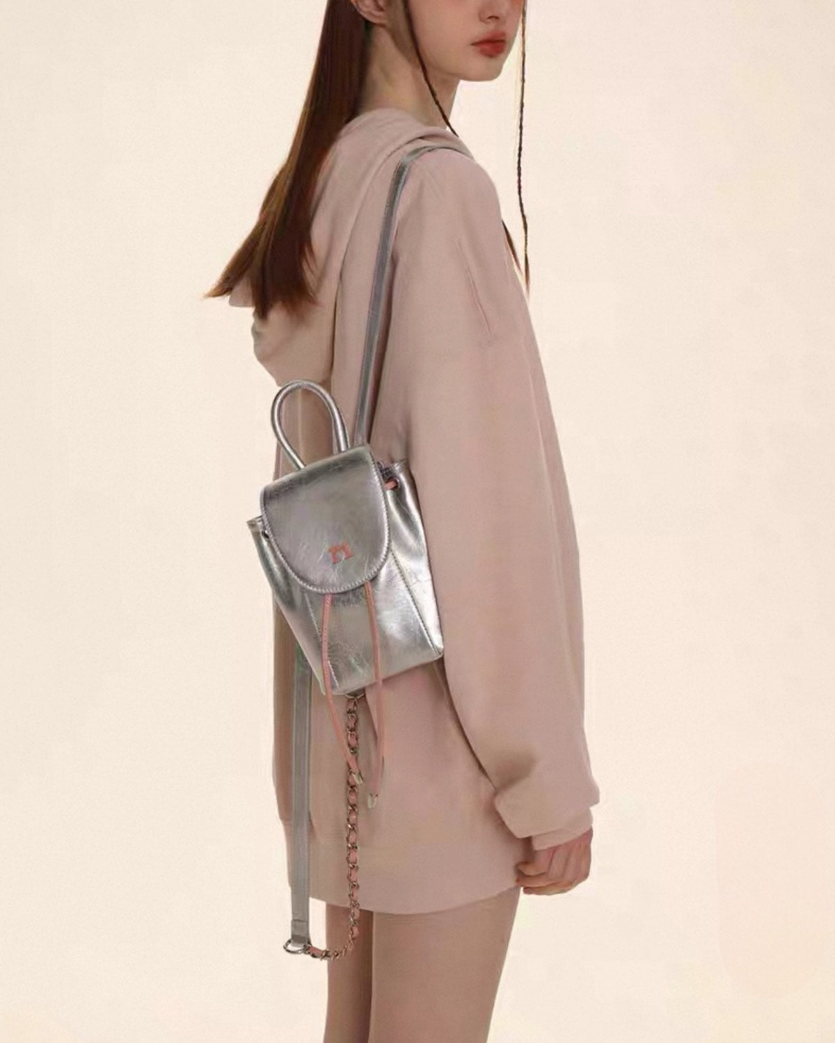 Person wearing a light pink outfit with a silver backpack on a beige background