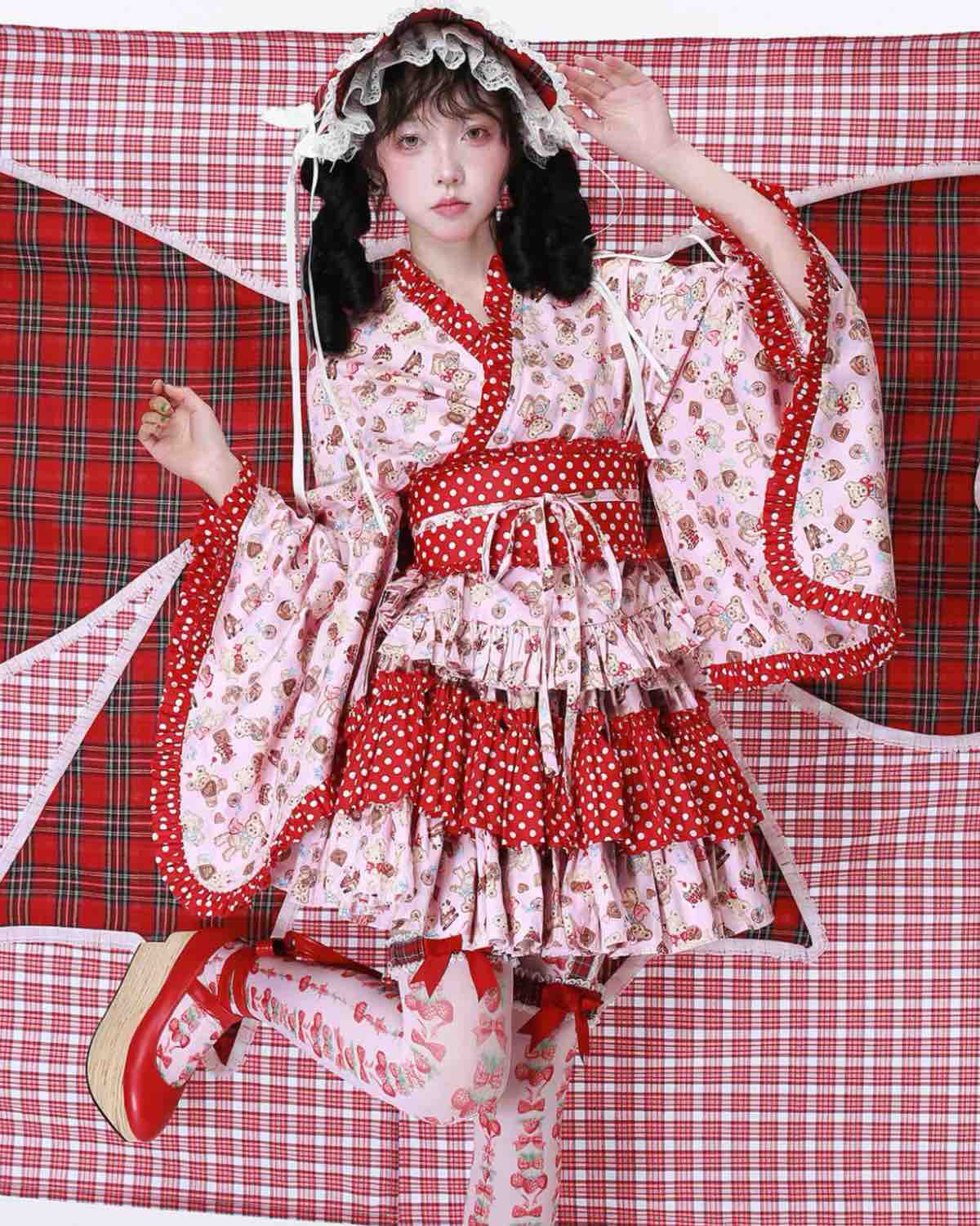 Person wearing a red and white polka dot dress with a matching headpiece against a red plaid background.