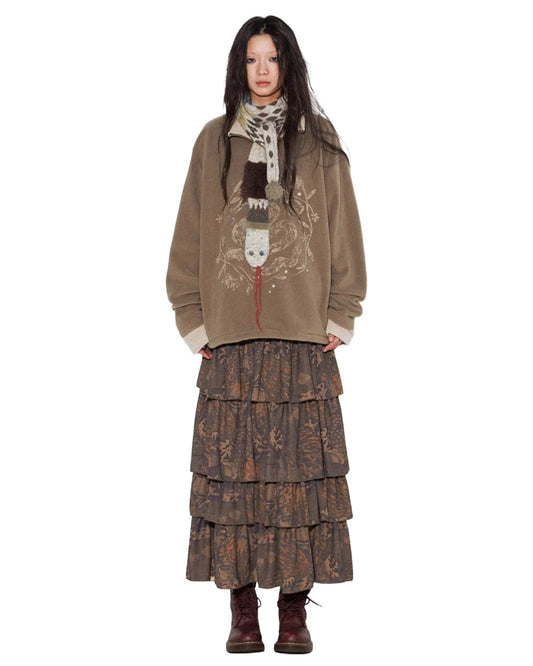 Person wearing a brown jacket with a pattern, layered skirt, and scarf on a white background