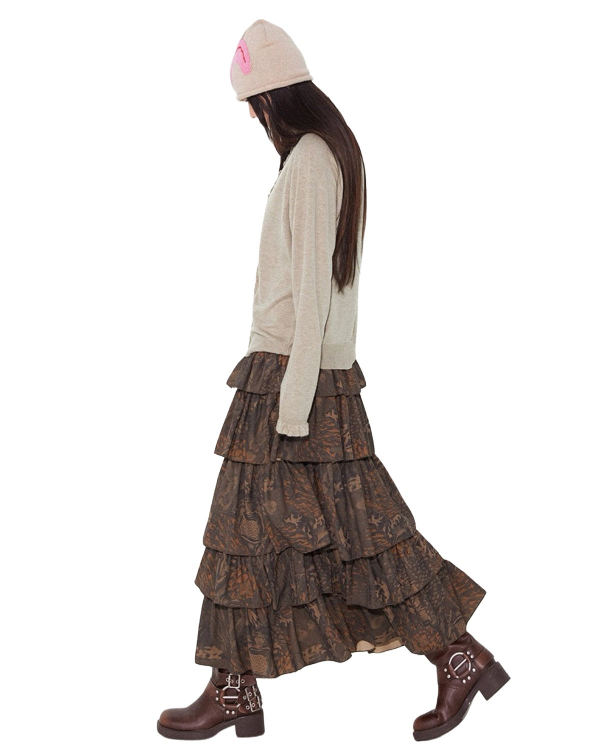 Person wearing a long, tiered brown skirt with a white top and pink beanie on a white background