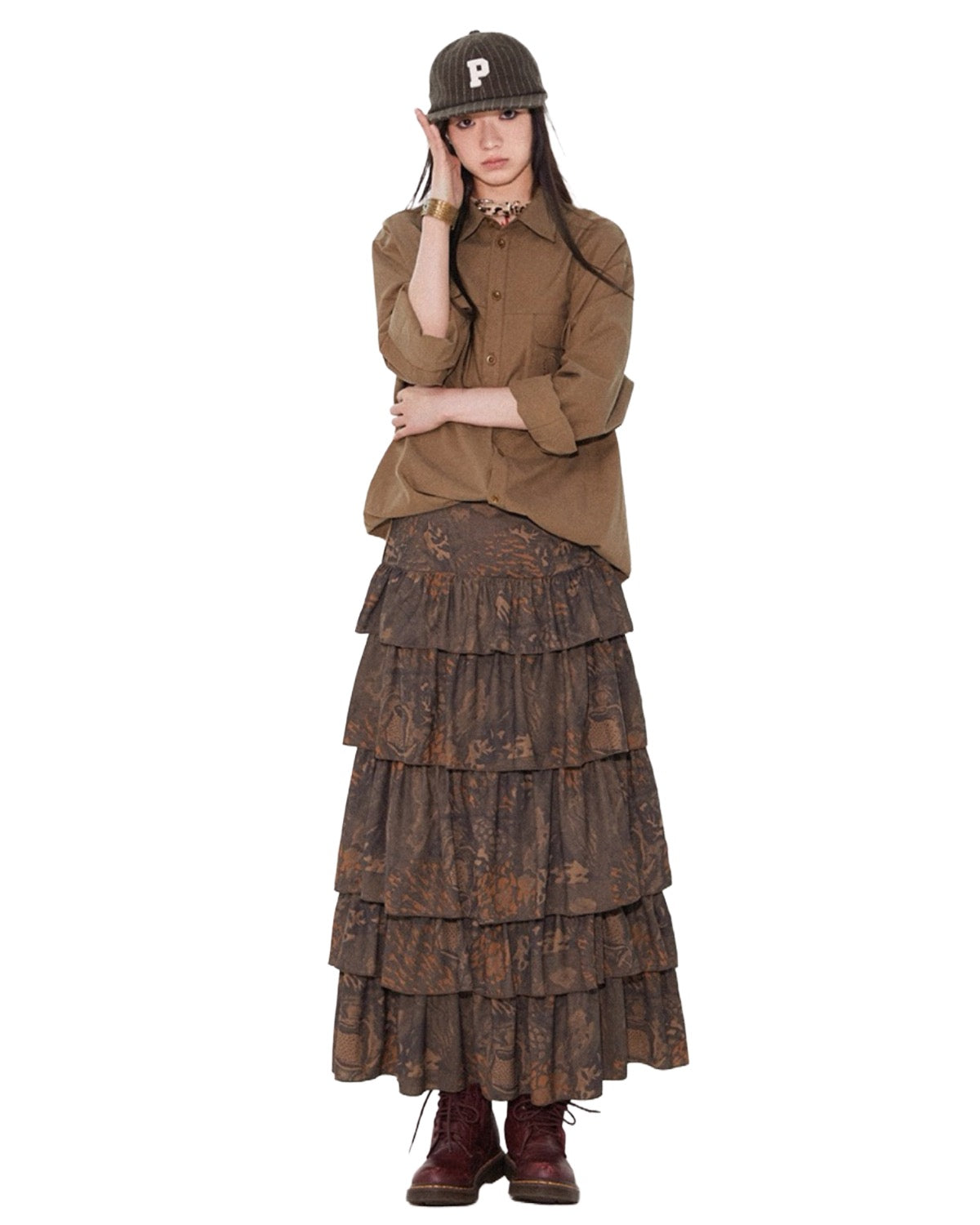 Woman wearing a brown jacket and tiered skirt with a cap on a white background