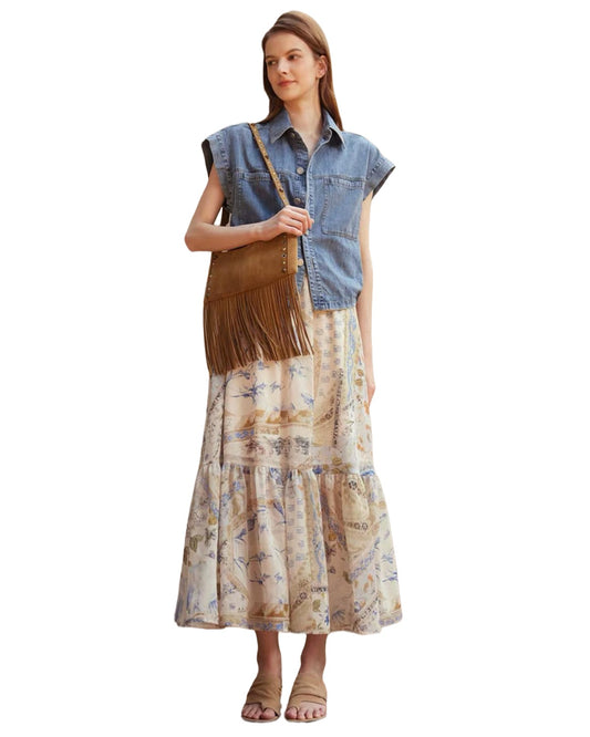 Woman wearing a denim shirt and patterned skirt with a brown fringed bag on a white background
