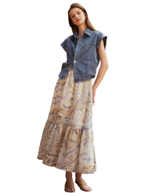 Woman wearing a denim sleeveless shirt over a long, patterned skirt on a white background
