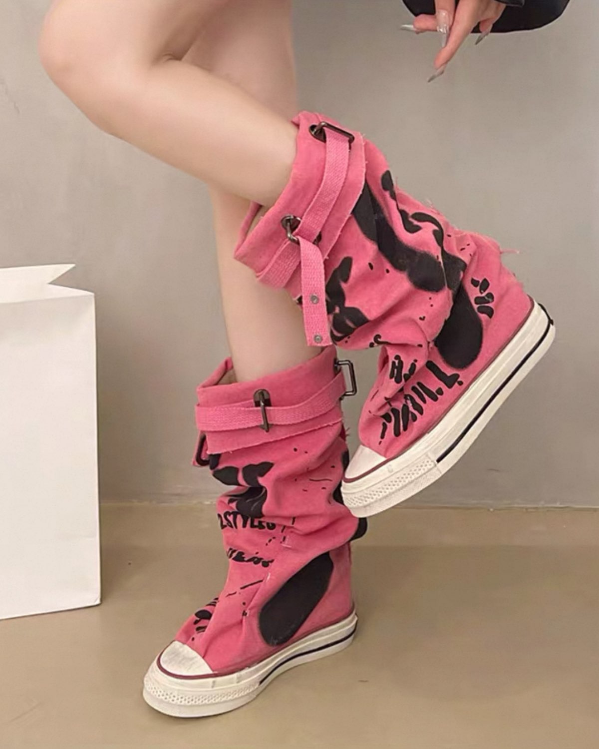 Pink high-top sneakers with black designs worn by a person on a neutral background