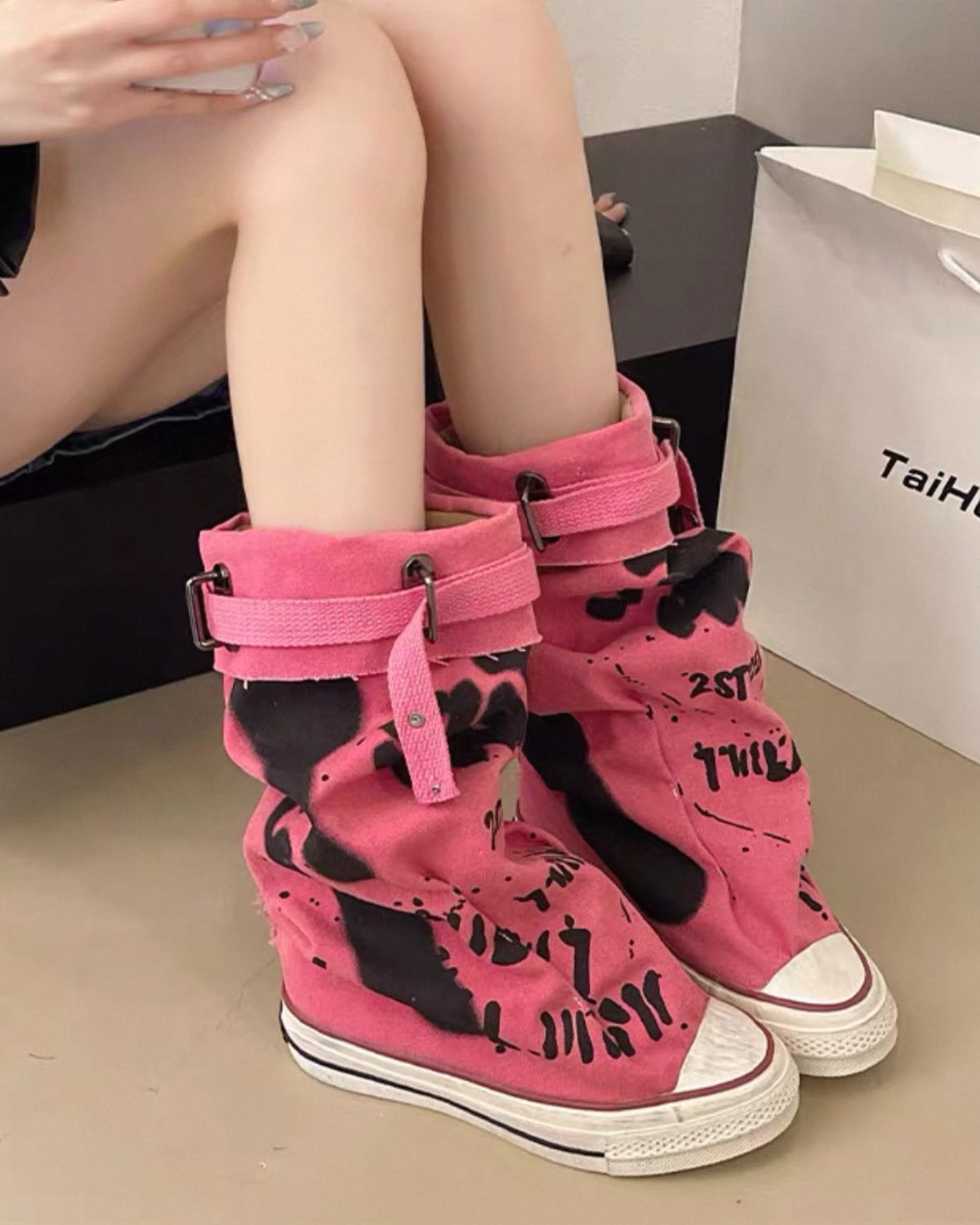 Pink high-top sneakers with black designs worn by a person sitting on a chair.