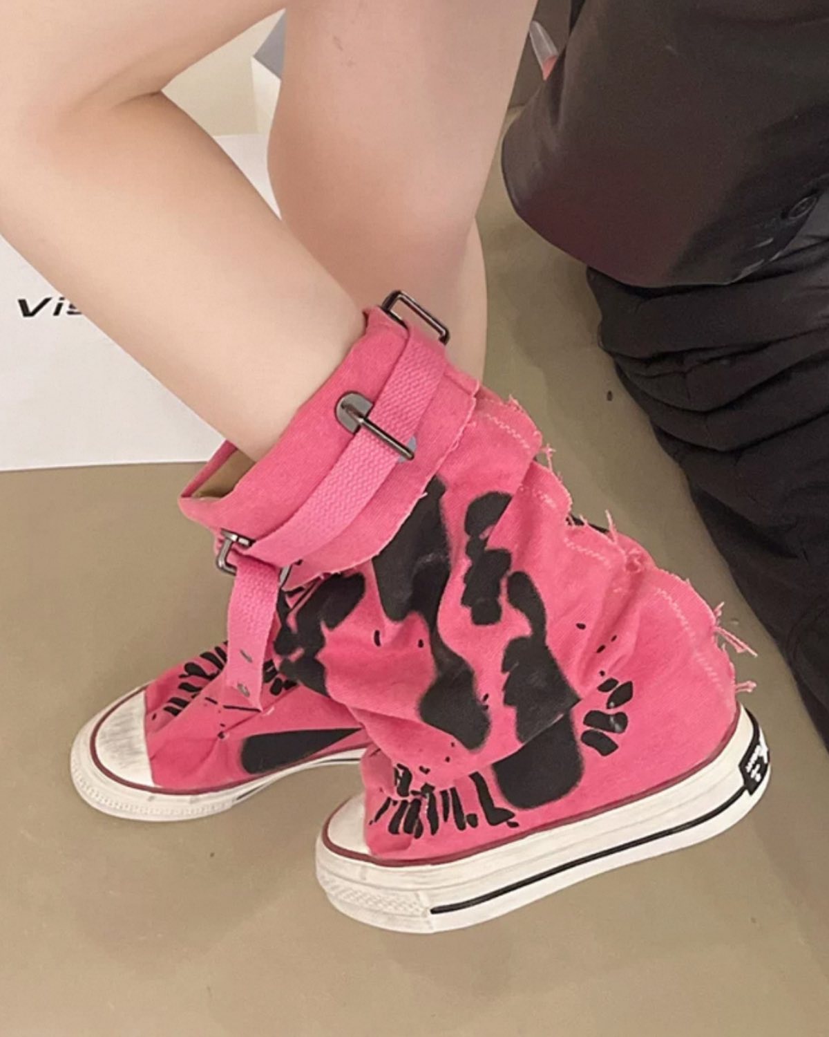 Pink sandals with black patterns worn by a child on a beige floor.