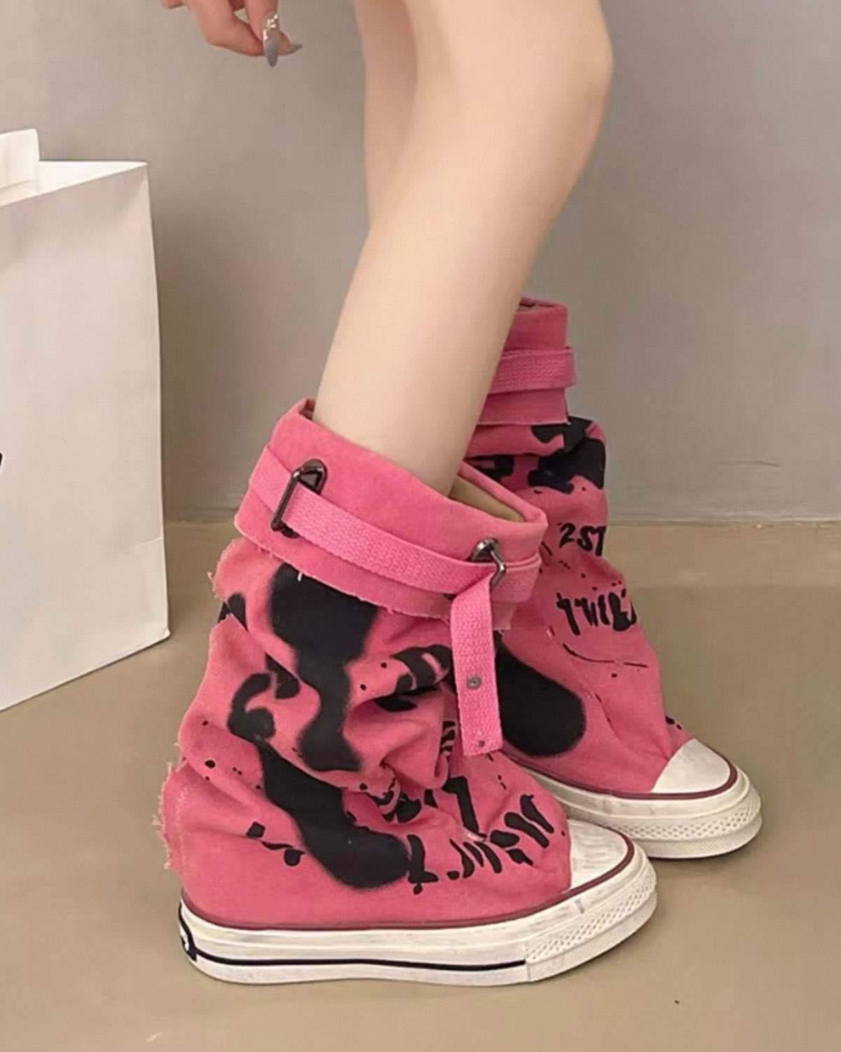 Pink high-top sneakers with black designs worn by a person on a neutral background