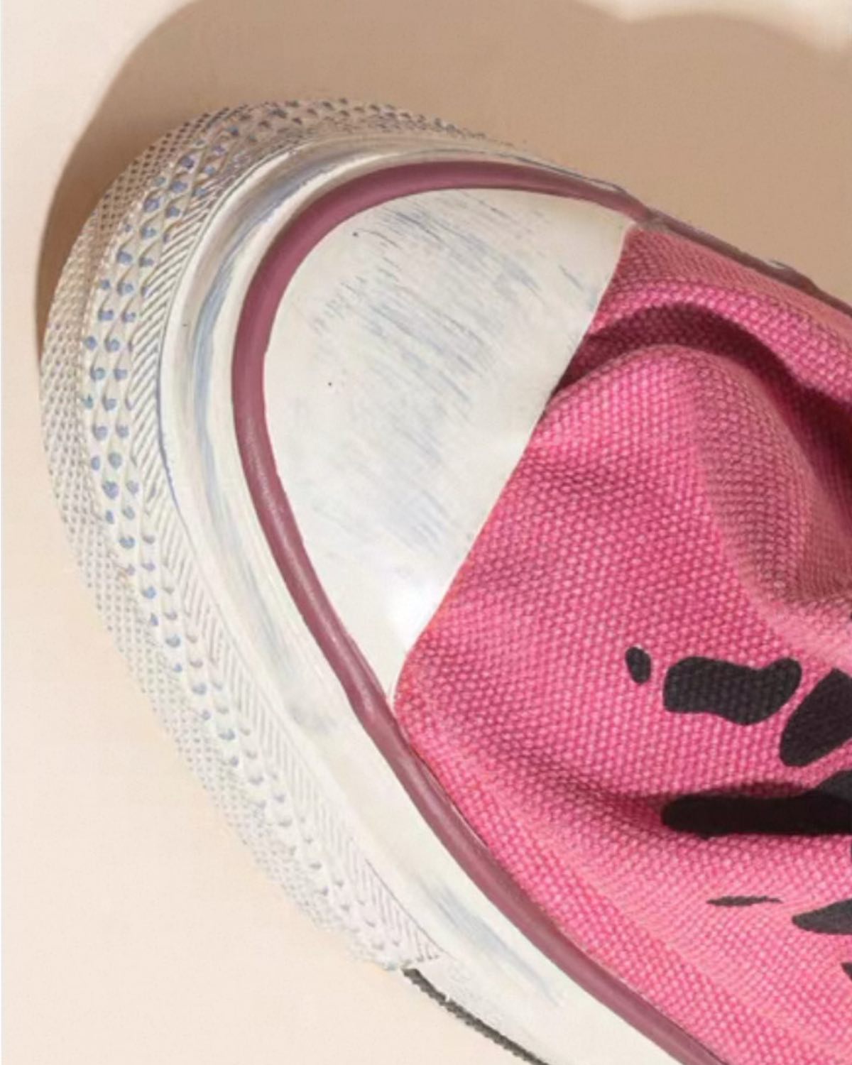 Close-up of a pink sneaker with a brand logo on a beige background
