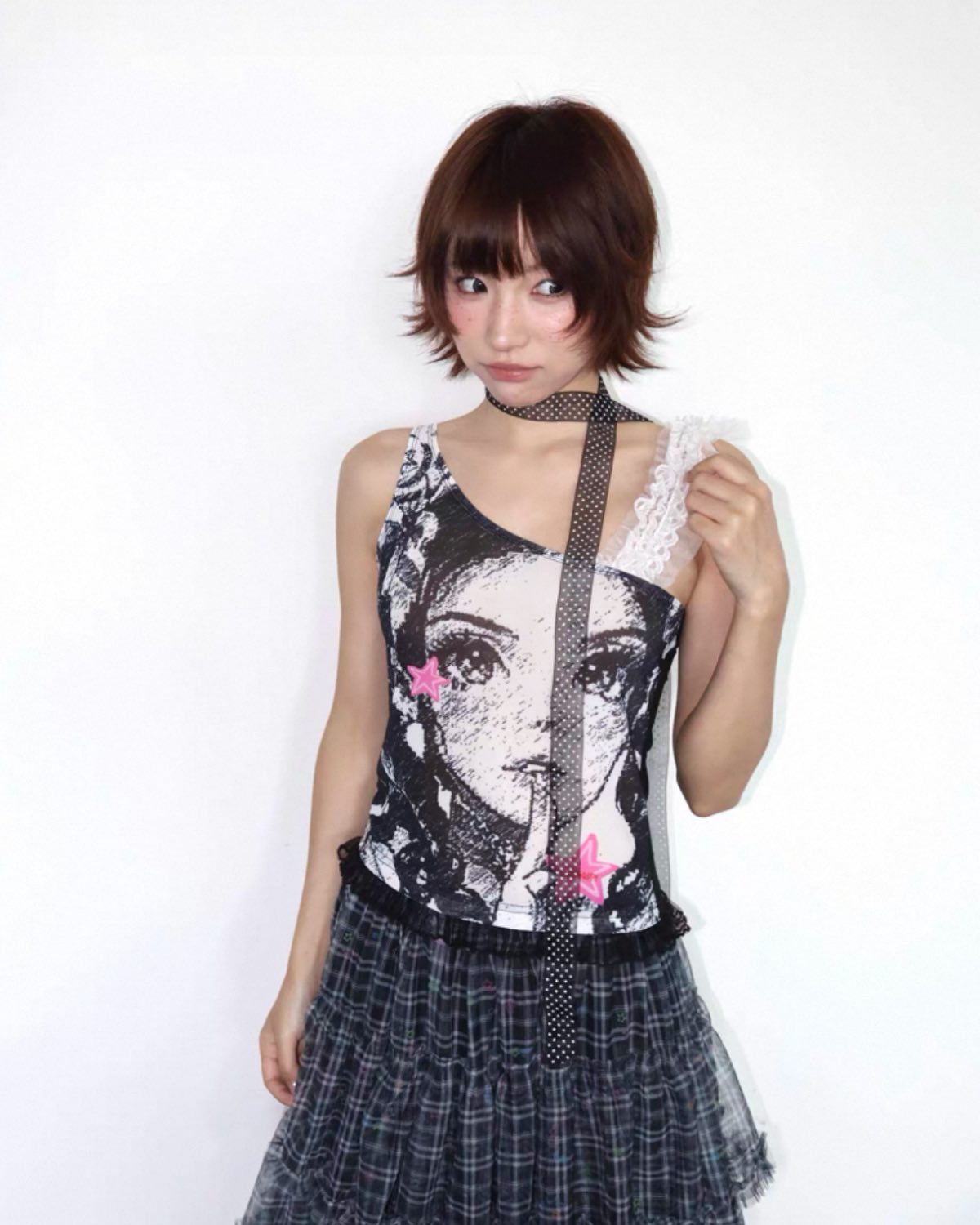Person wearing a sleeveless top with a graphic design and a plaid skirt on a white background