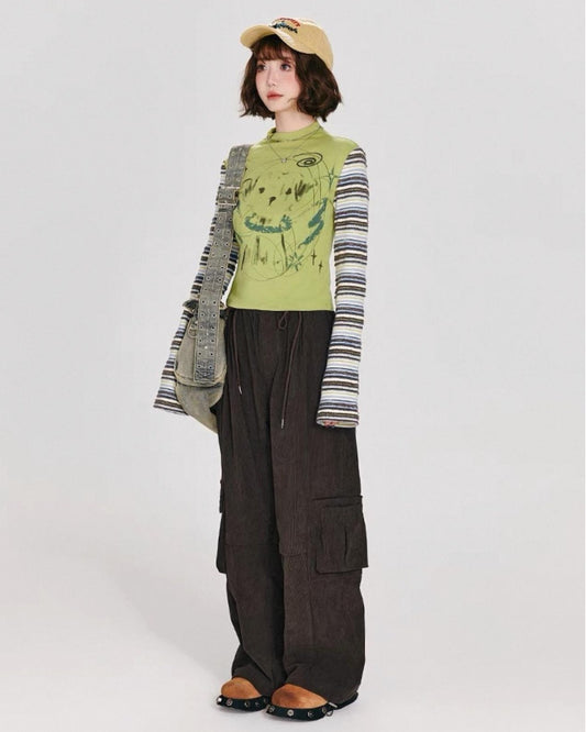 Person wearing a green graphic tee, dark cargo pants, and a beige cap on a white background