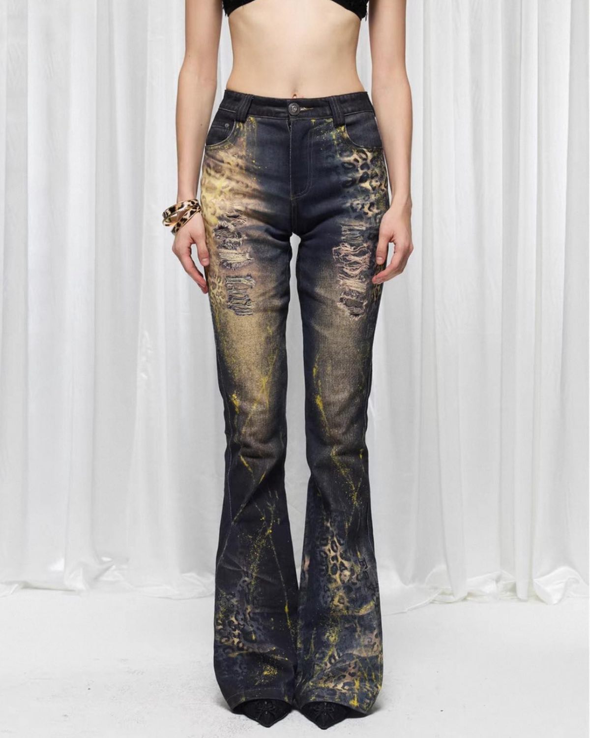Person wearing distressed black and gold flared jeans on a white background
