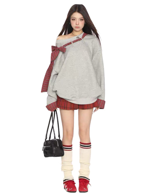 Woman wearing a gray sweater with plaid accents and red skirt on a white background