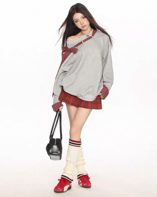 Person wearing a gray oversized sweater with red accents, a red plaid skirt, and white knee-high socks with red stripes.