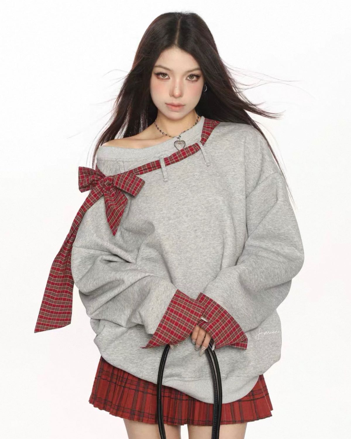 Person wearing a gray oversized sweatshirt with red plaid accents on a white background