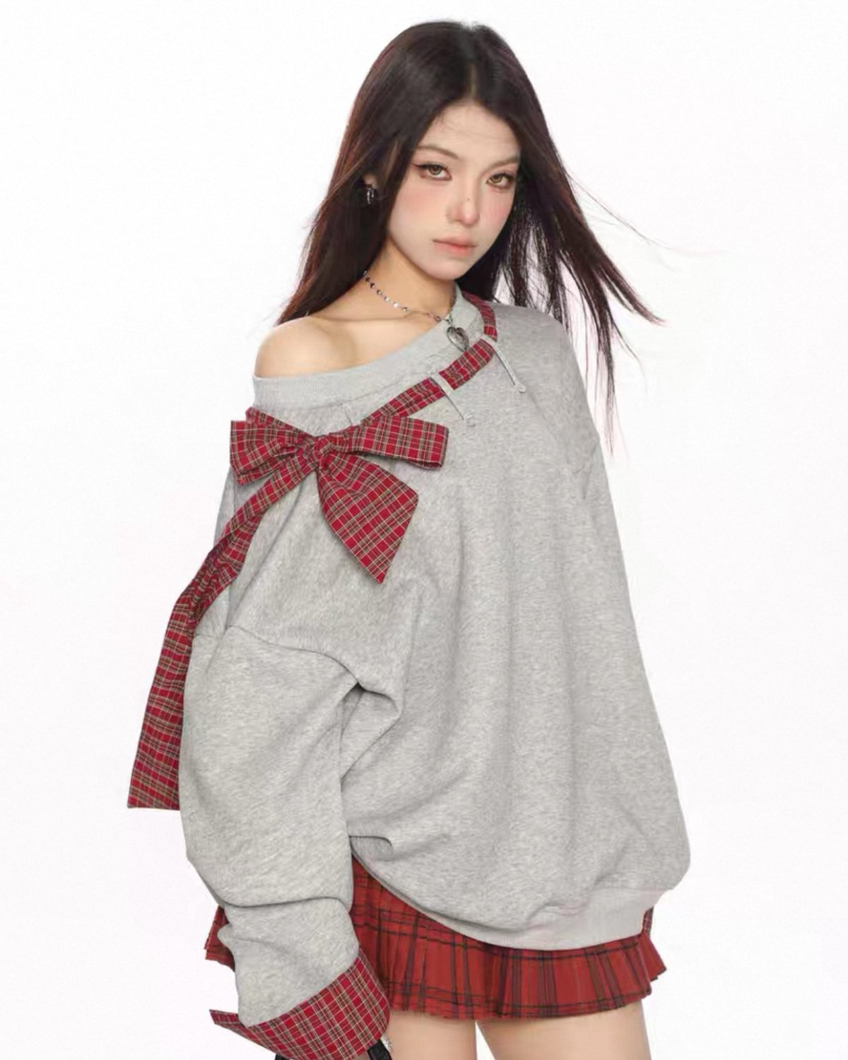Woman wearing a gray sweatshirt with a red plaid bow and skirt on a white background