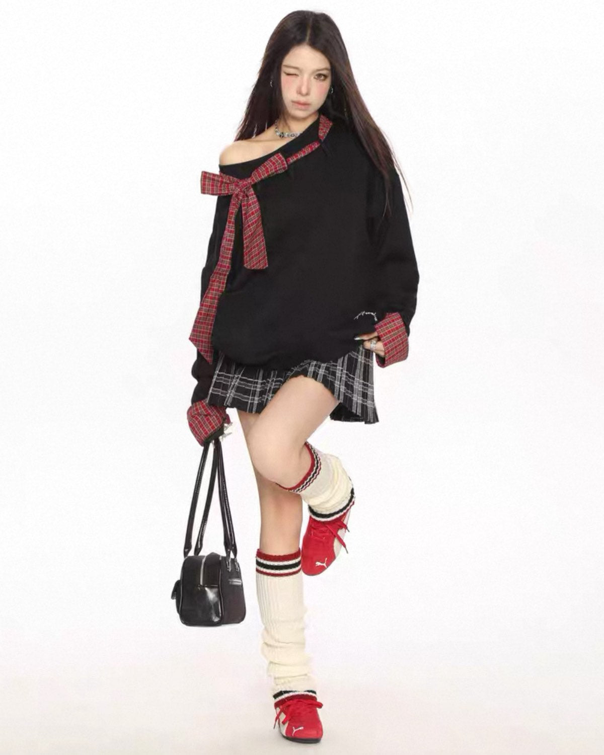 Person wearing a black oversized sweater with red accents, plaid skirt, and knee-high socks on a white background
