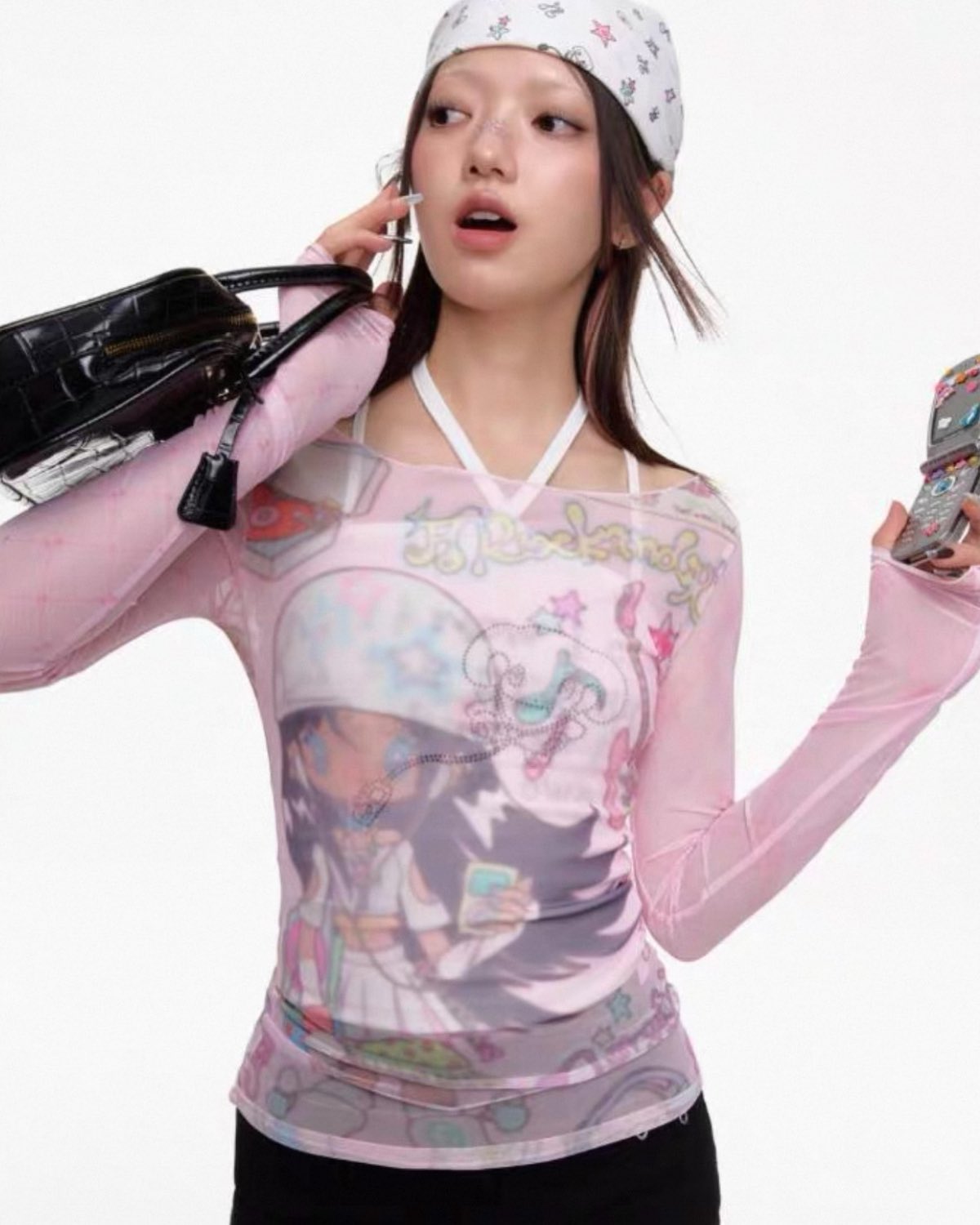 Woman wearing a pink long-sleeve shirt with graphic design, holding a phone and a bag on a white background