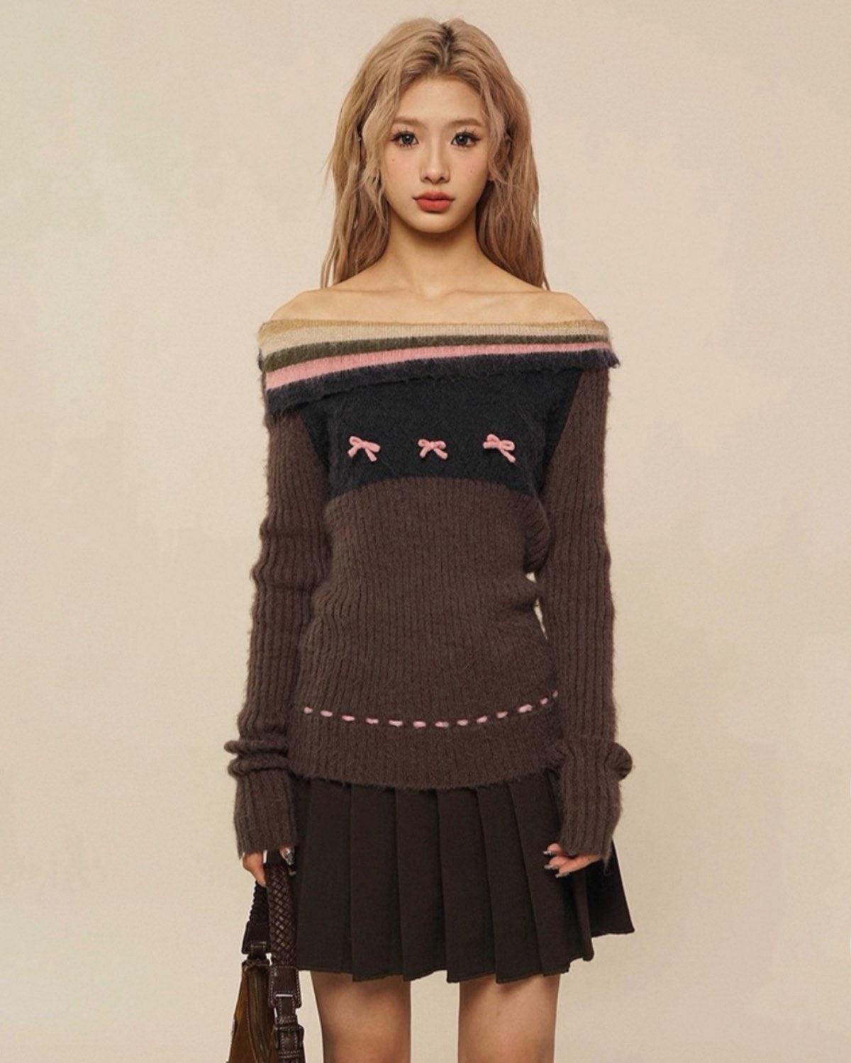 Woman wearing a brown off-shoulder sweater with pink accents and a pleated skirt on a beige background
