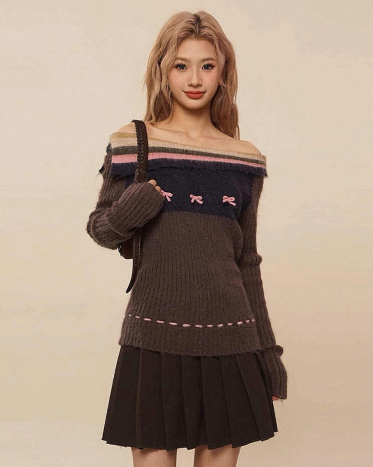 Woman wearing a brown off-shoulder sweater with pink accents and a black pleated skirt on a beige background