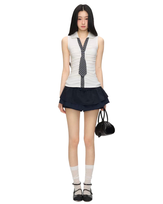 Woman wearing a sleeveless top with a tie design and a navy skirt on a white background