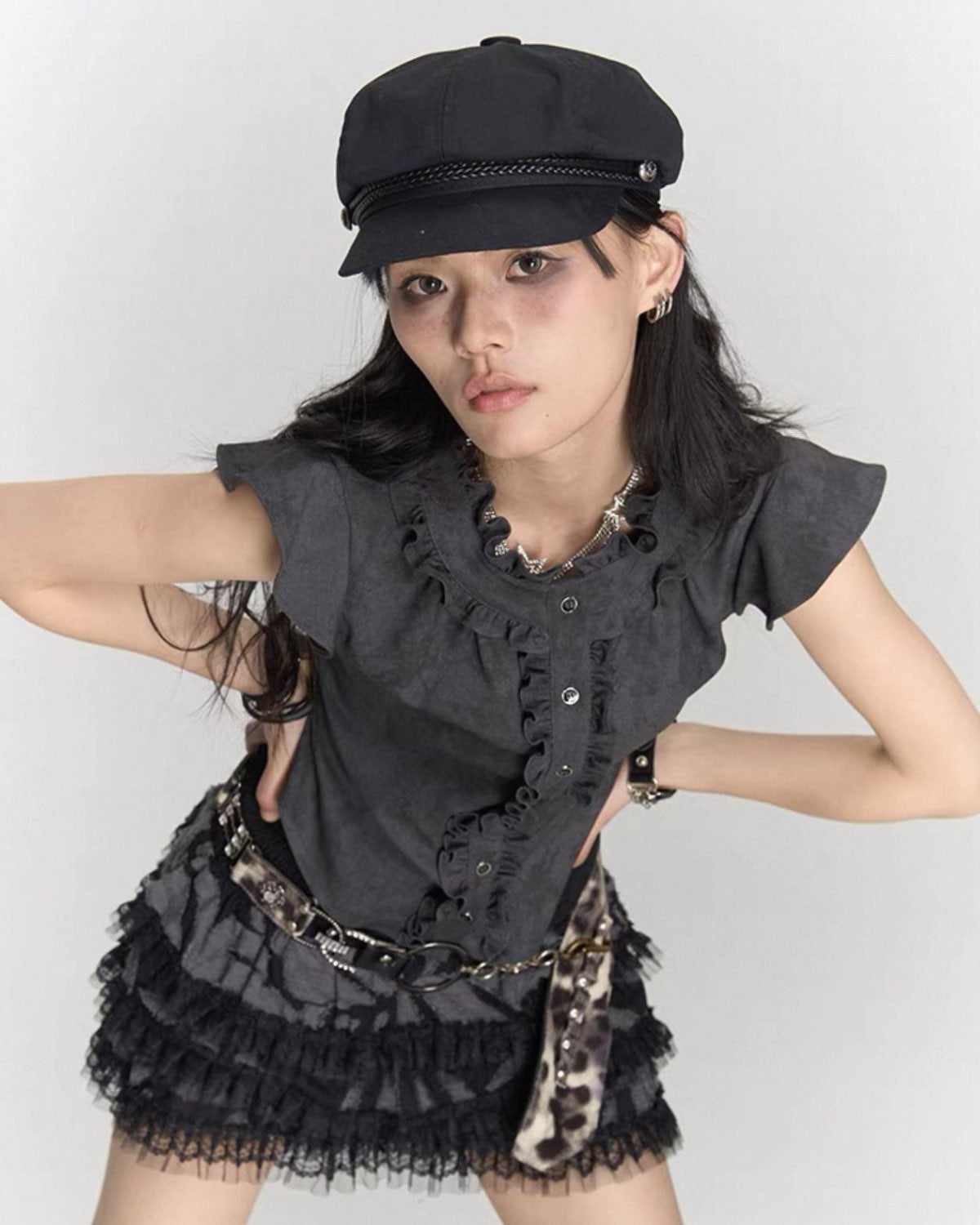 Woman wearing a black outfit with ruffled details and a cap on a white background