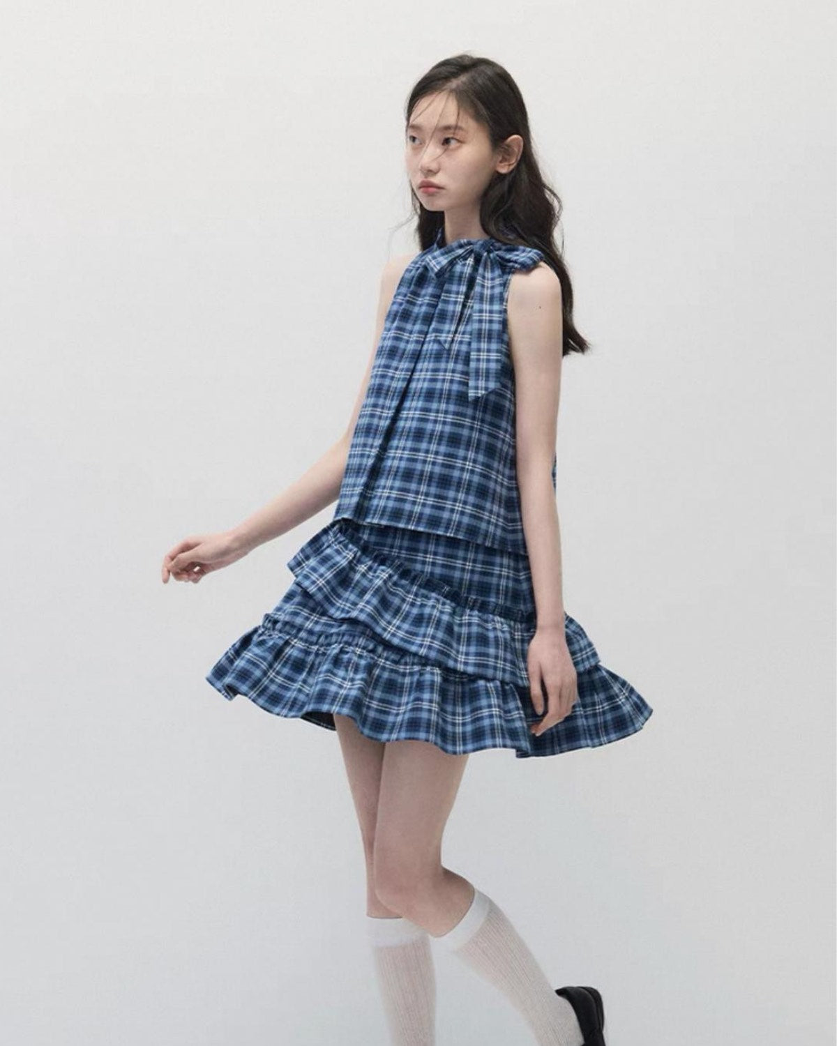 Woman wearing a blue plaid dress and swirling against a white background