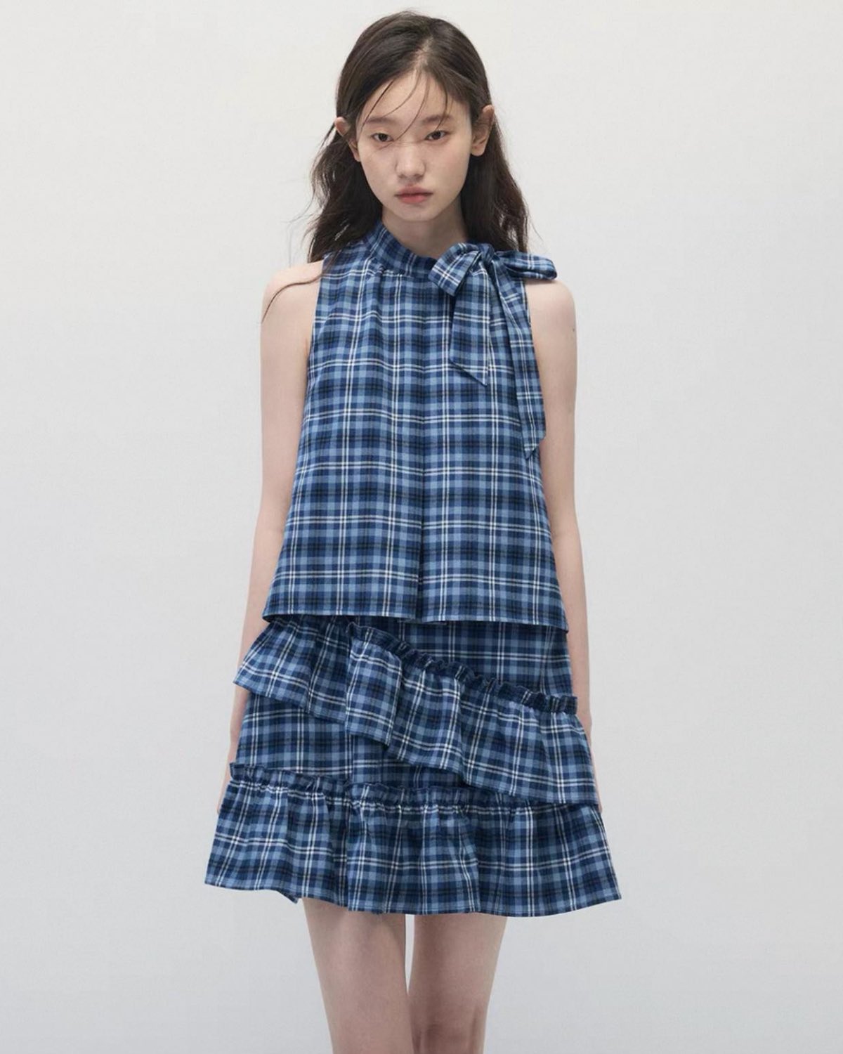 Young girl wearing a blue plaid dress closer up against a plain background