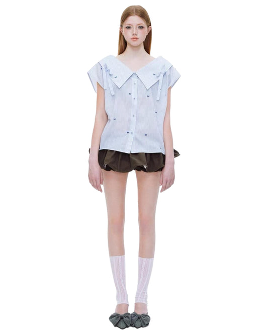 Model wearing a light blue ruffled blouse and black shorts on a white background