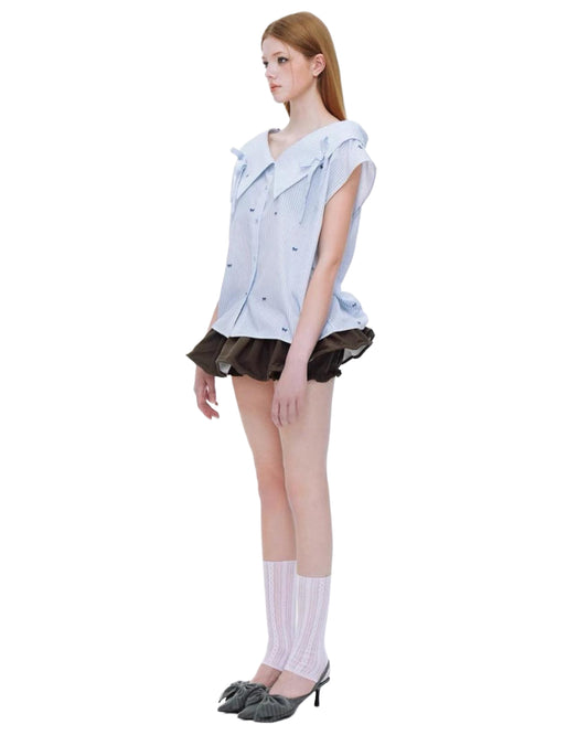 Model wearing a light blue sleeveless shirt with a brown skirt on a white background side view