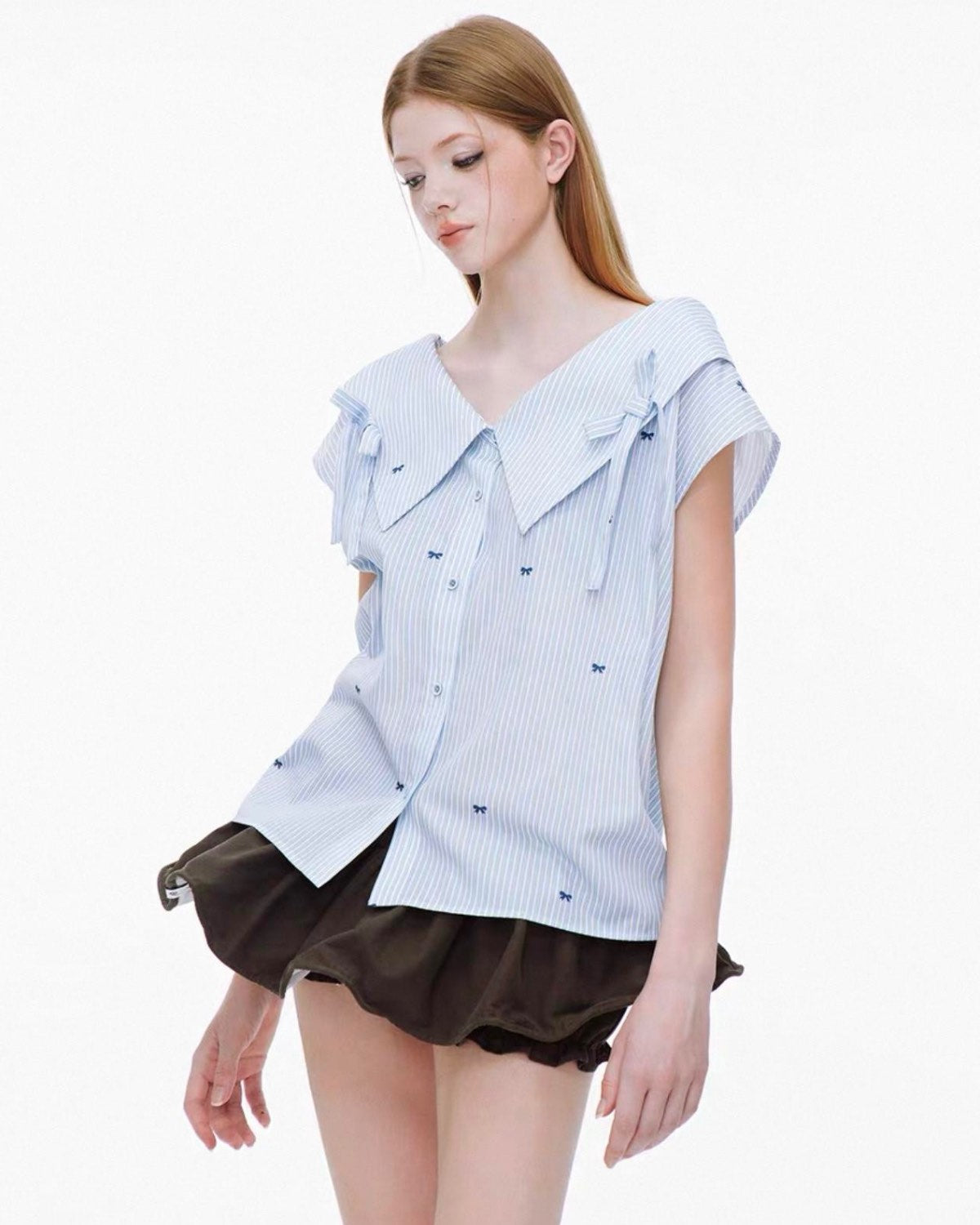 Woman wearing a light blue ruffled blouse and brown shorts on a white background