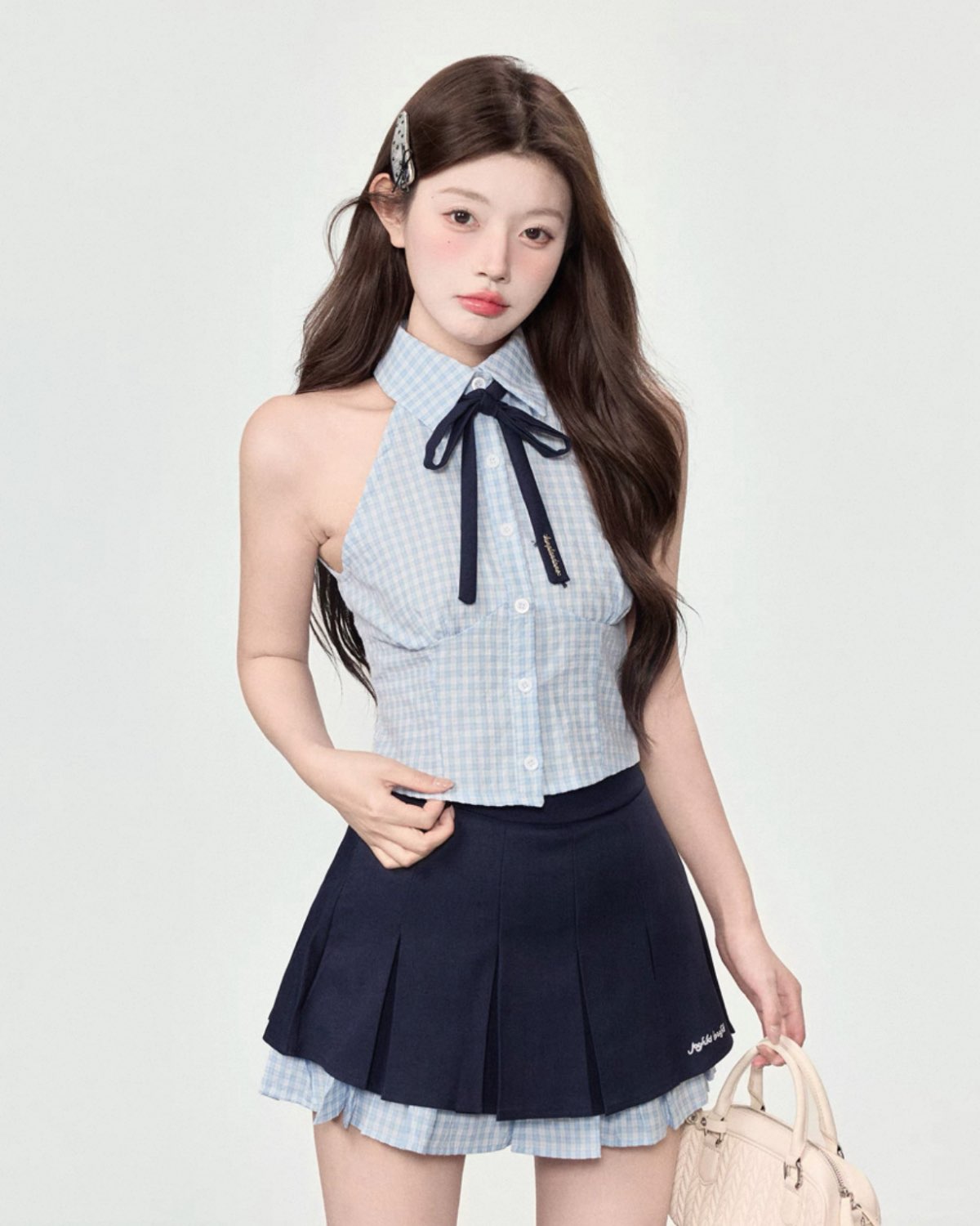 Woman wearing a checkered top with a bow and navy pleated skirt on a white background
