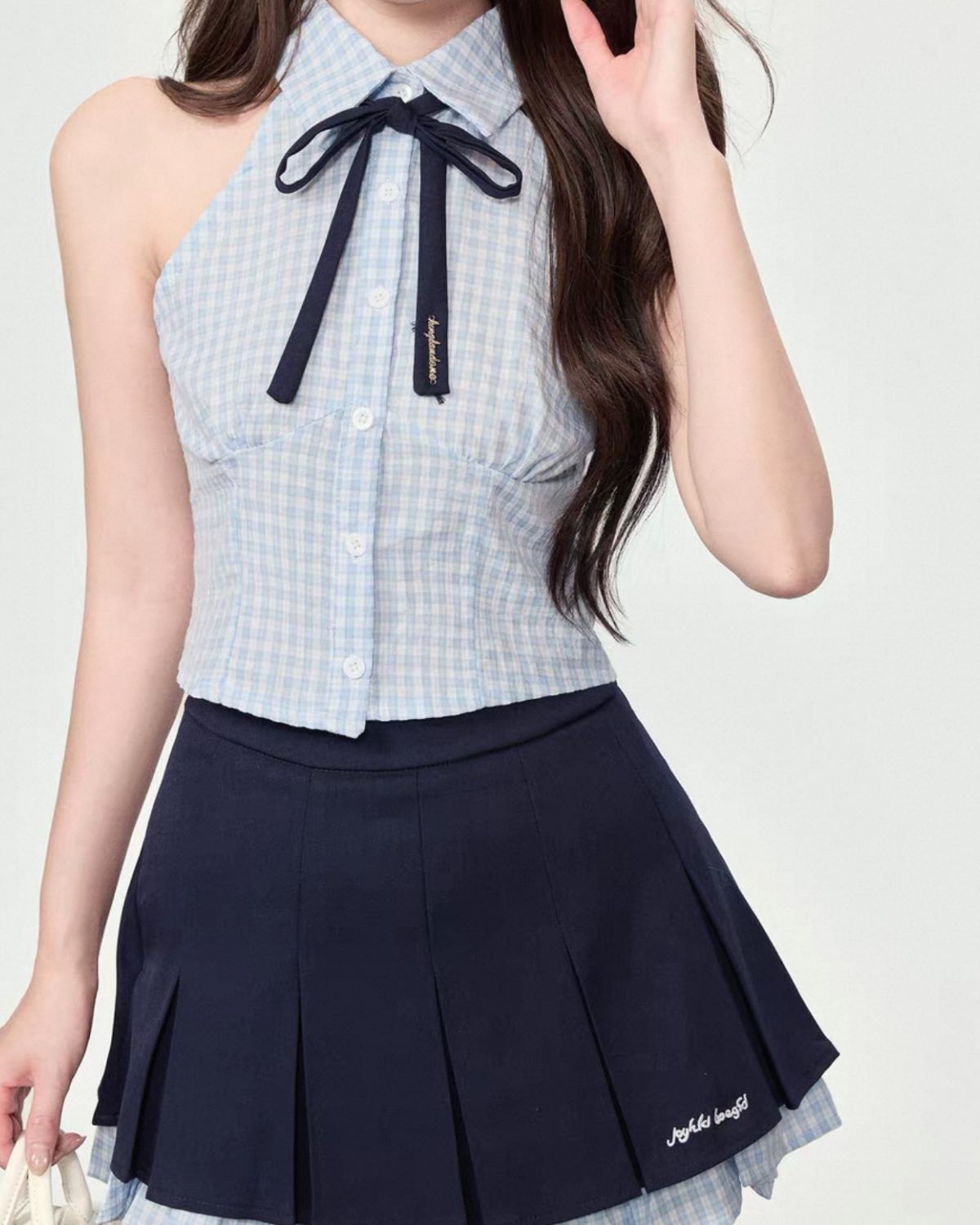 Person wearing a checkered top with a bow and a navy pleated skirt on a white background
