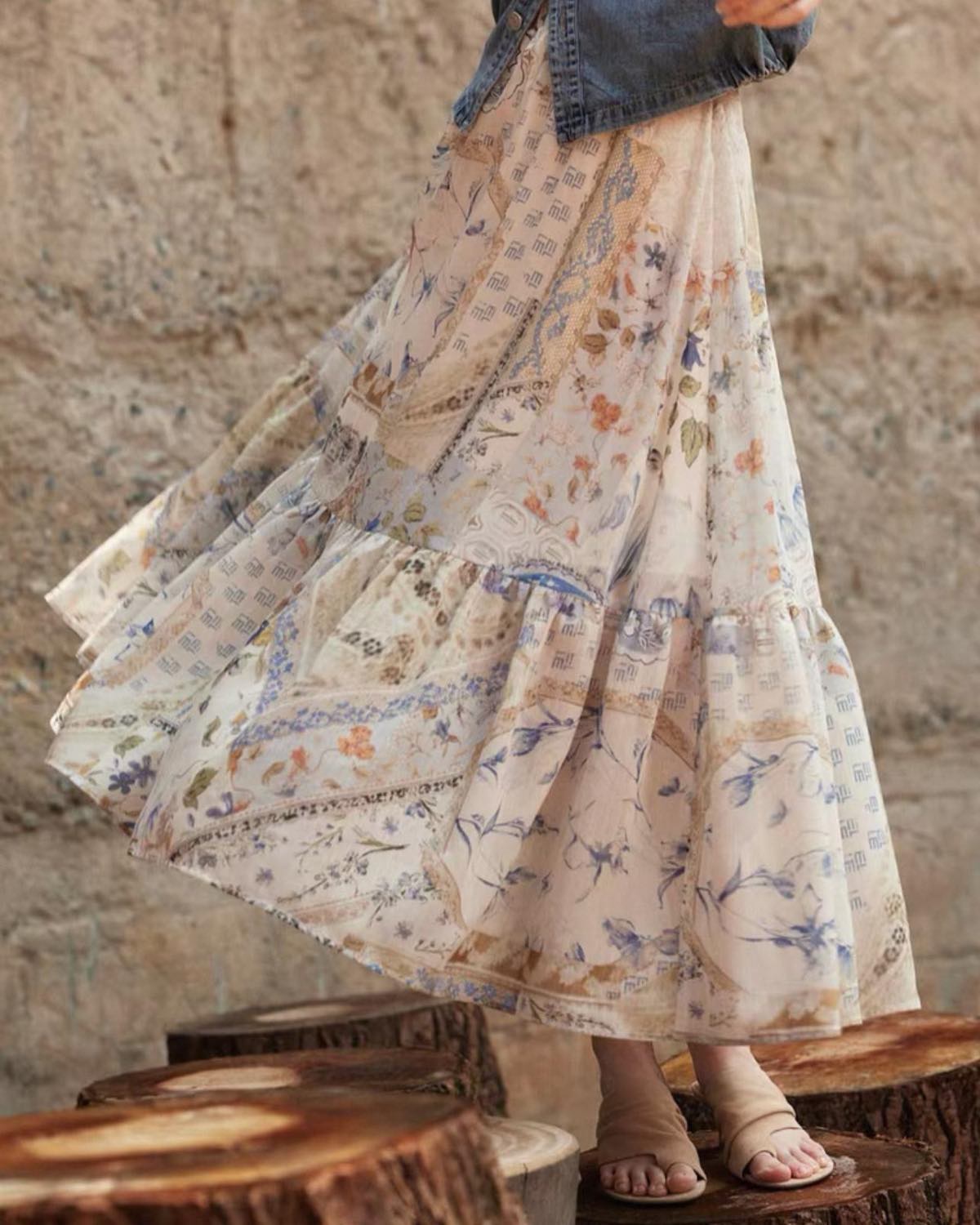 Person wearing a long, flowing floral skirt against a stone wall.
