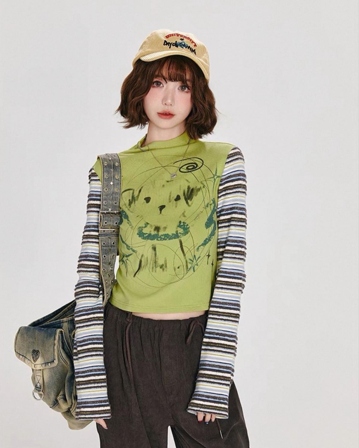 Person wearing a green graphic hoodie, striped long-sleeve shirt, and brown pants with a beige cap. Focus on Top.