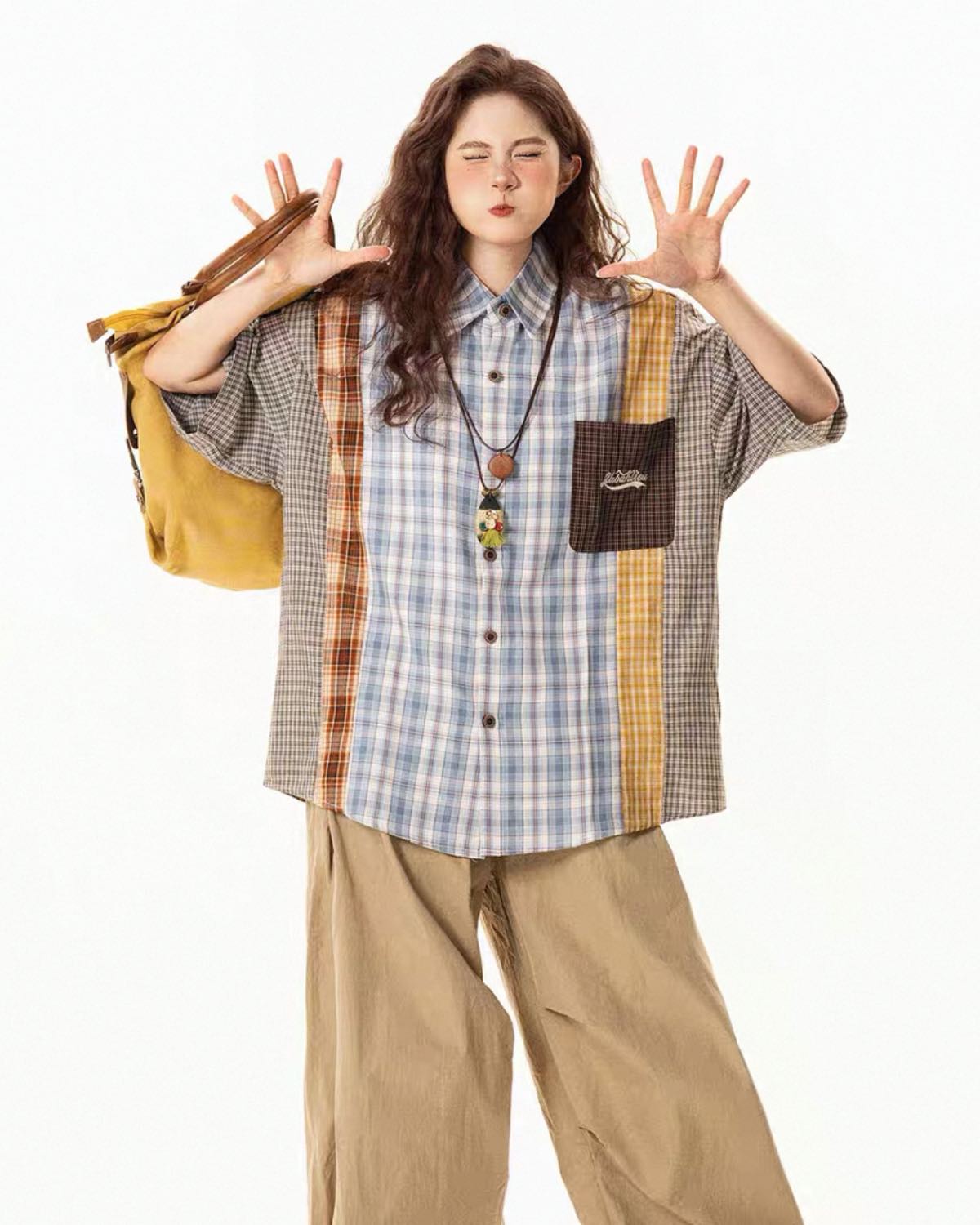 Person wearing a plaid shirt with a yellow bag and beige pants on a white background