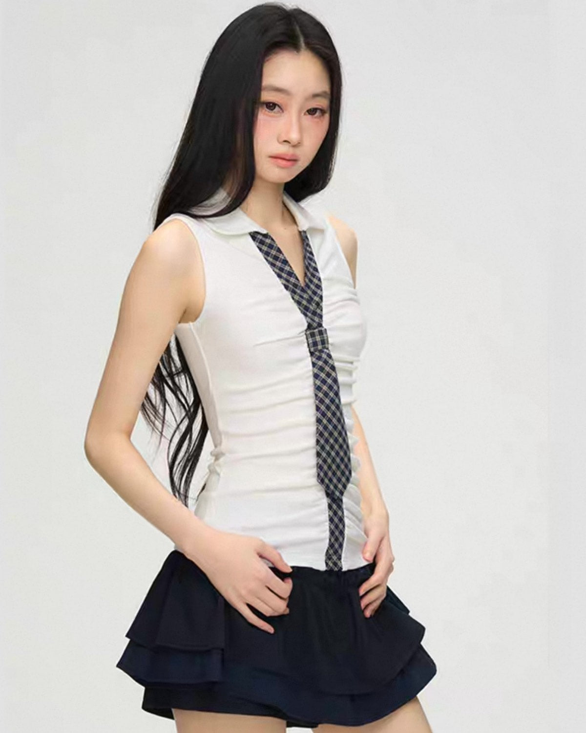 Woman wearing a white sleeveless top with a plaid tie and a navy blue skirt on a white background