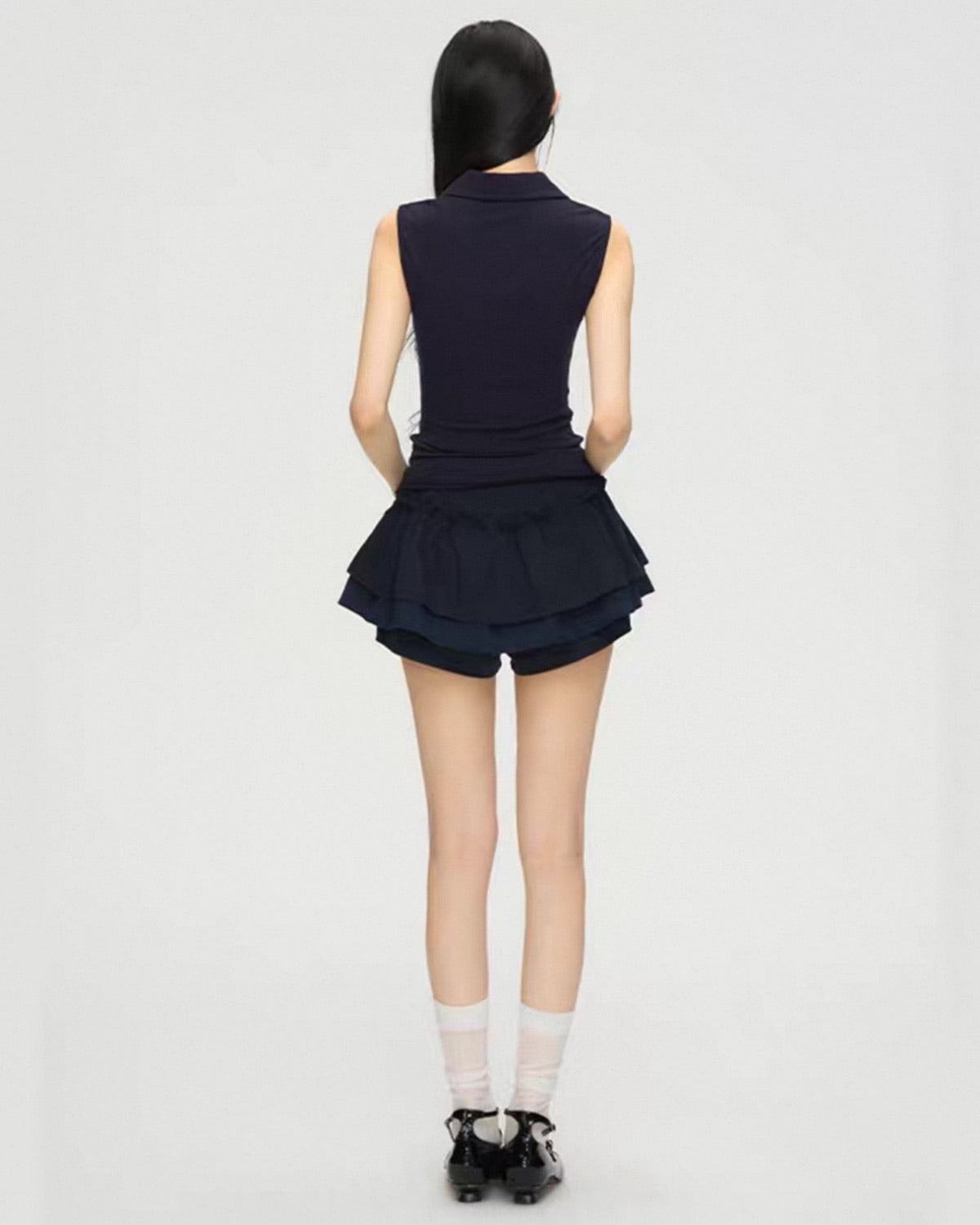 Person wearing a navy blue sleeveless top and skirt on a white background